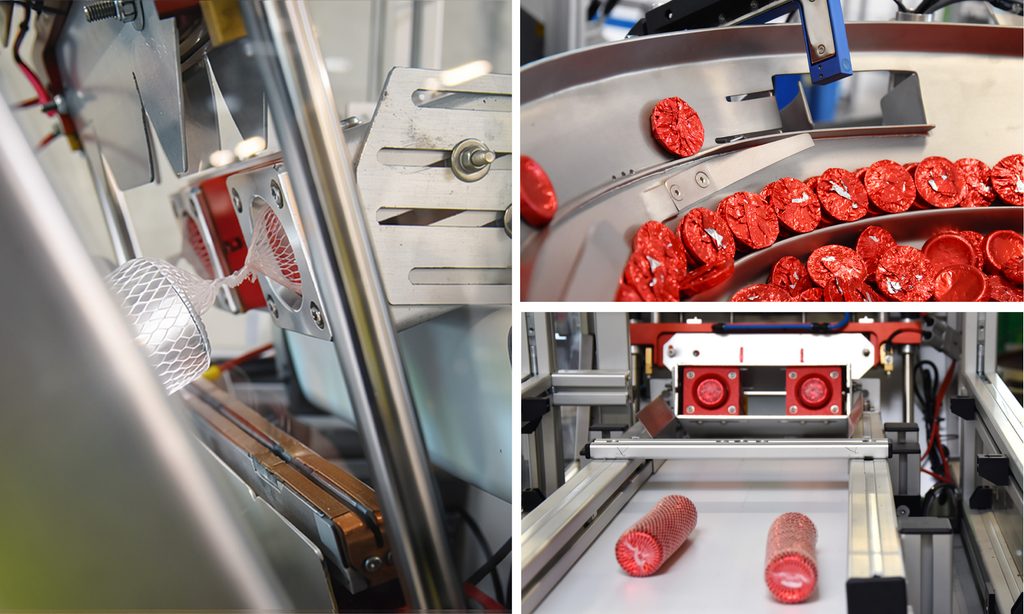 Automated manufacturing line with metal guides and red, snail-shaped capsules on a conveyor belt forming a curved track.
